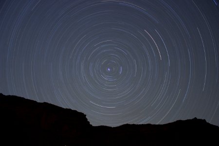 Concentric circles created by stars moving through the night sky over a silhouetted rock face photo