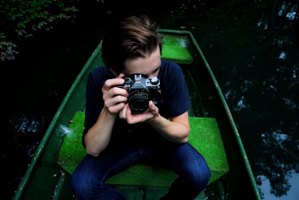 man in black t-shirt and blue denim jeans riding on row boat holding bridge camera on focus photo