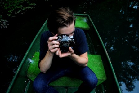 man in black t-shirt and blue denim jeans riding on row boat holding bridge camera on focus photo