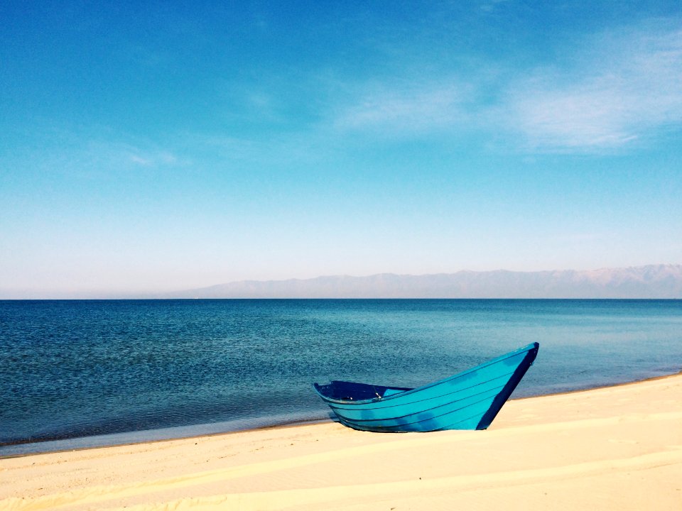blue boat on sand near body of water during daytime
