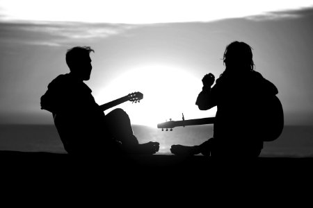 Two figures silhouetted against the sun, laughing with musical instruments photo