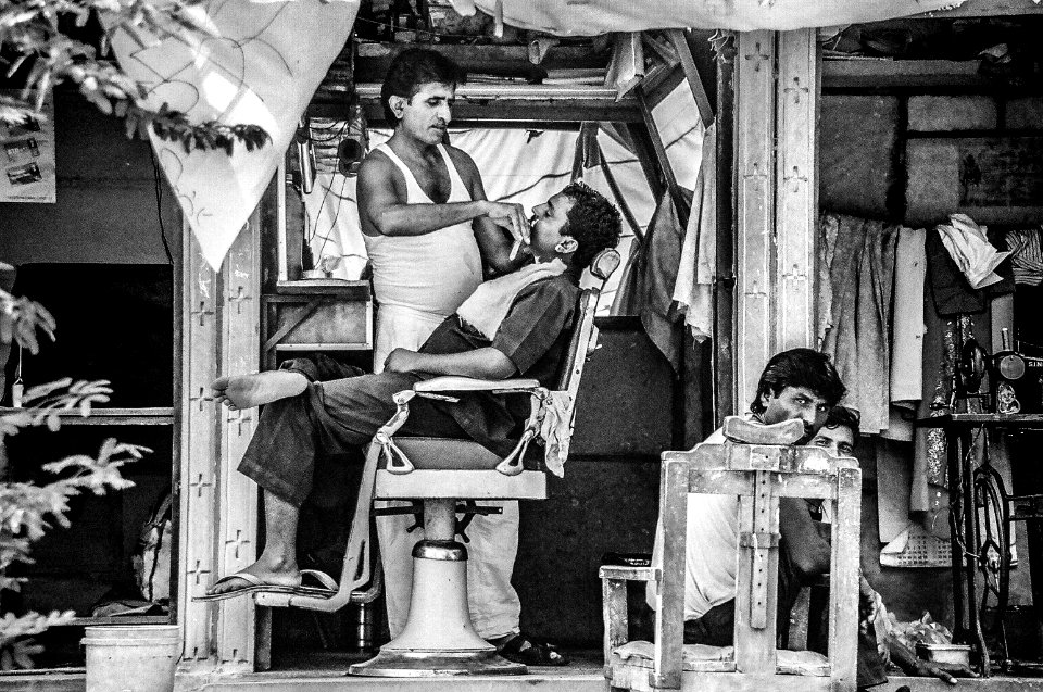 grayscale photo of barber trimming man's beard