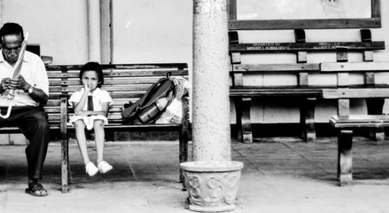 grayscale photography of man holding umbrella sitting on bench beside girl photo