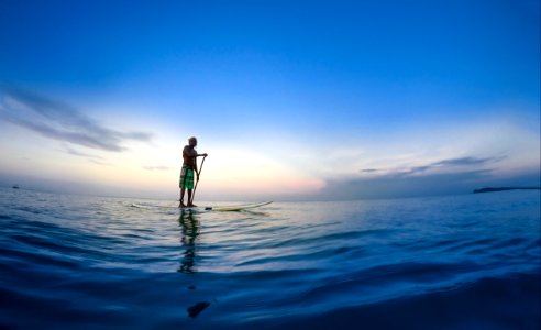 man standing on white paddle board holding paddle on body of water under blue sky photo