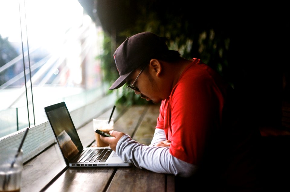 man holding phone in with laptop beside cup