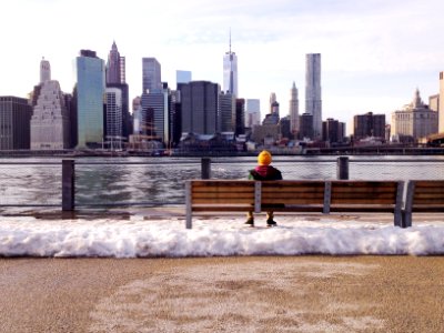 person in knit cap sitting on wooden bench in front of body of water during daytime photo