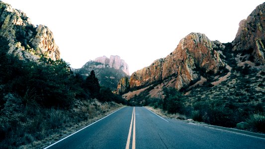 road lined with rocky mountain at daytime photo