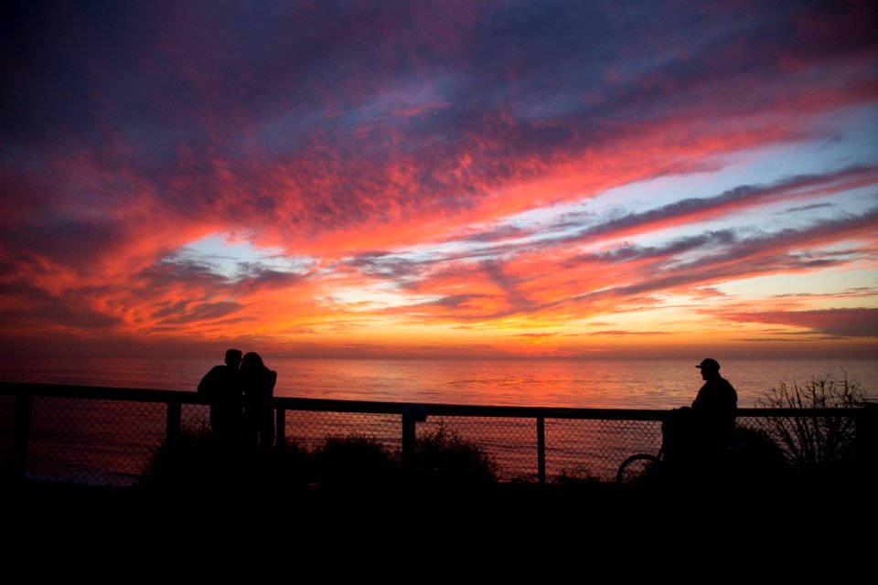 silhouette of people near cliff railings at distance to wide body of water during golden hour