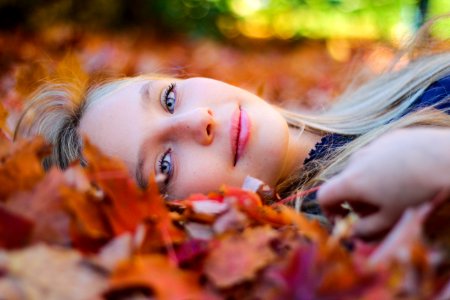 woman wearing blue top lying on dried maple leaves during daytime photography photo
