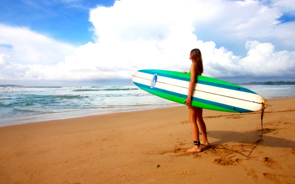woman standing near sea holding white, blue, and green surfboard under blue sky