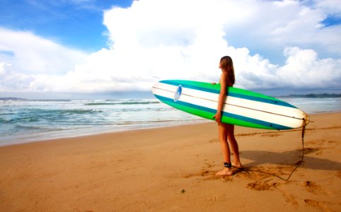 woman standing near sea holding white, blue, and green surfboard under blue sky photo