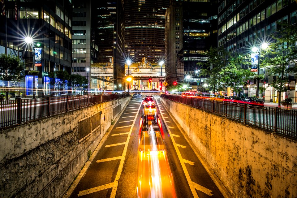 time lapse photography of vehicle passing on concrete road surround high-rise buildings during night time