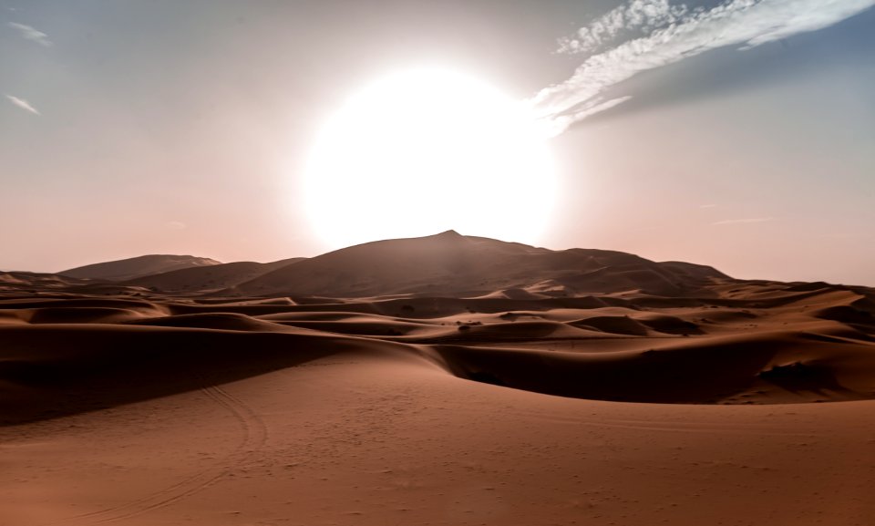Sun rides over rolling sand dunes of the Sahara Desert