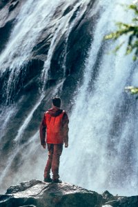 man standing on rock facing waterfall photo