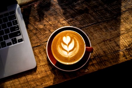 caffe latte on white ceramic cup beside silver and black laptop computer photo