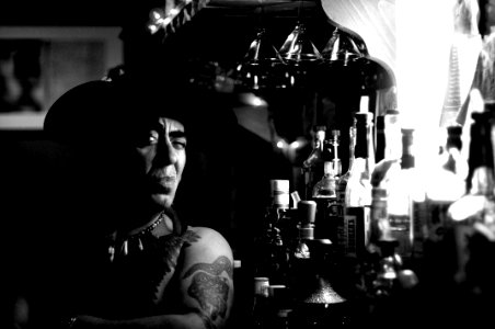 man wearing hat beside bottles on grayscale photography