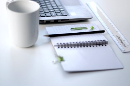 black pencil on ruled notepad beside white ceramic mug and gray laptop computer photo