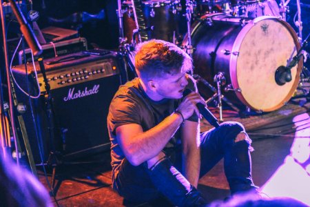 vocalist man holding microphone sitting in front of Marshall guitar amplifier near drum kit photo