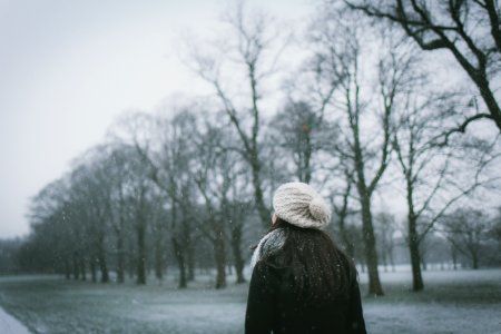woman wearing cap and black coat standing near bare tree photo