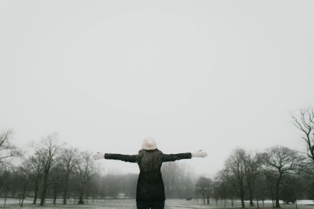 woman in black long-sleeved shirt standing and facing trees with stretched arms under white sky photo