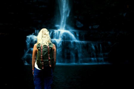 shallow focus photography of woman with backpack in front of water falls photo