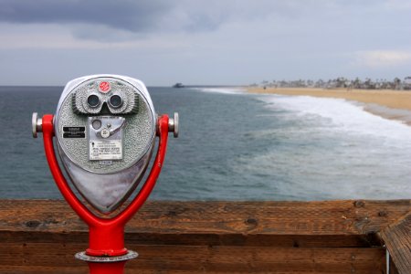grey and red coin operated binoculars in front of seawaves under nimbus clouds during daytime