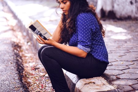 woman sitting on gutter reading book photo