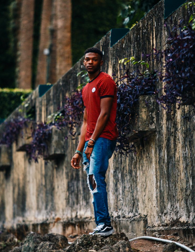 An African American man in ripped jeans and a red striped shirt.