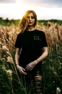 selective focus photography of black crew-neck t-shirt and distressed black bottom standing on brown wheat field during daytime