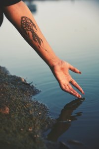 person hand reaching calm water with dreamcatcher tattoo photo