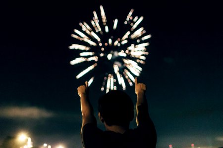man in black shirt pointing towards brocade fireworks in the skies