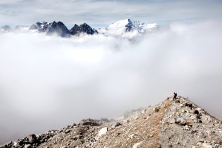person standing on peak front of white clouds and ice-capped mountain photo