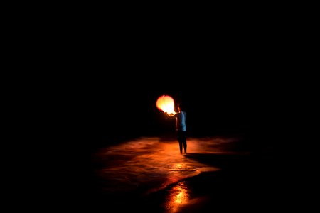 person standing on shore holding brown paper lantern photo
