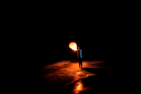 person standing on shore holding brown paper lantern