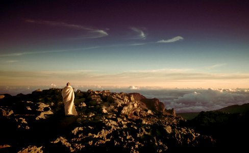 person wearing white robe on top of rocky mountain photo