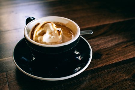 white and black ceramic mug filled with brown latte on round black ceramic saucer photo