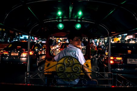 man in white collared shirt sitting in yellow and black autorickshaw between cars with taillights turned on at night