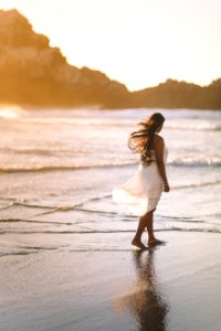 selective focus photo of woman standing on sea shore near rock formation during golden hour photo