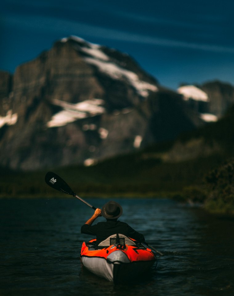 man riding on inflatable kayak beside mountain