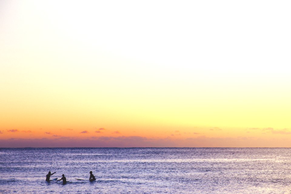 three person playing on ocean during golden hour
