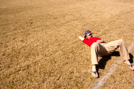man in red top lying on lawn field during daytime