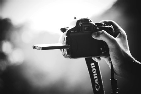 grayscale photography of person holding Canon DSLR camera photo