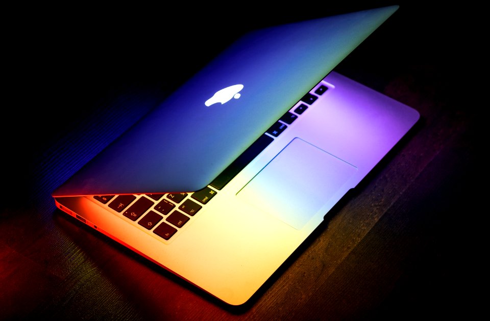 A MacBook lit up in rainbow colors on a wooden surface