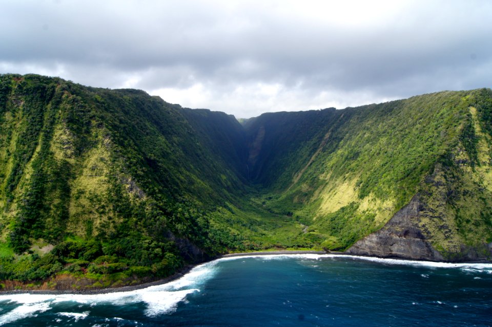 green dense mountain beside body of water under white cloudy sky at daytime