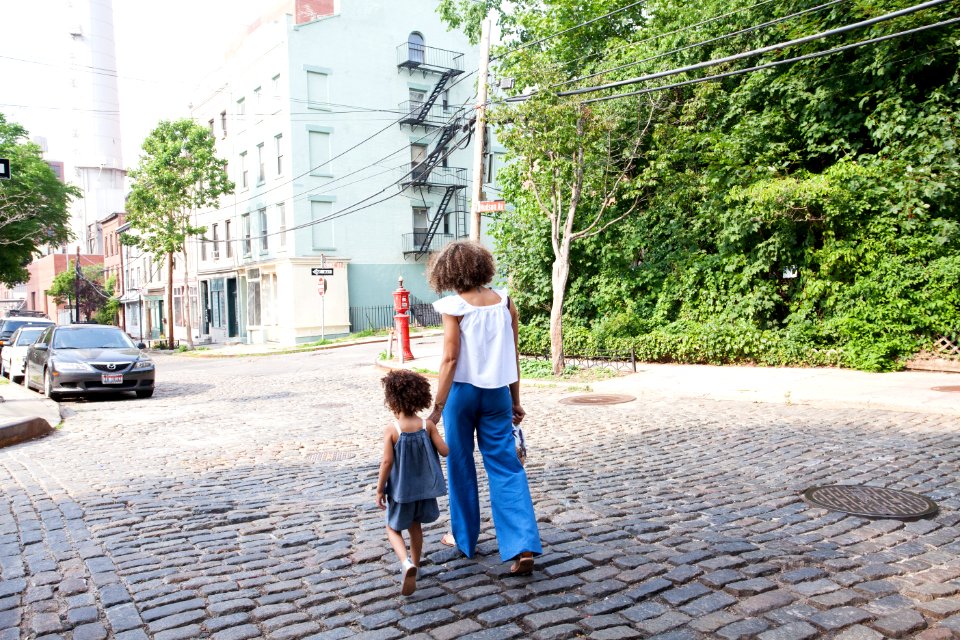 woman in white cap-sleeved shirt and blue pants walking beside girl in gray tank top