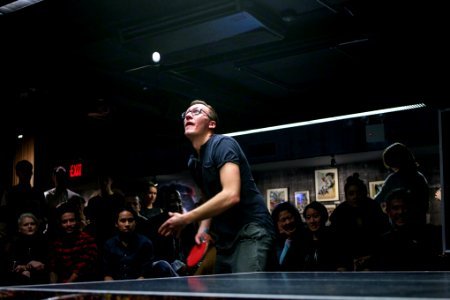 man about to paddle ping pong ball surrounded by group of people photo