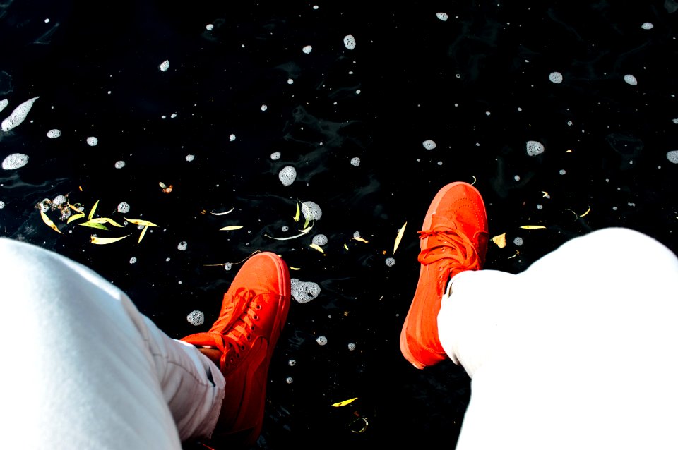 person wearing orange sneakers sitting near water