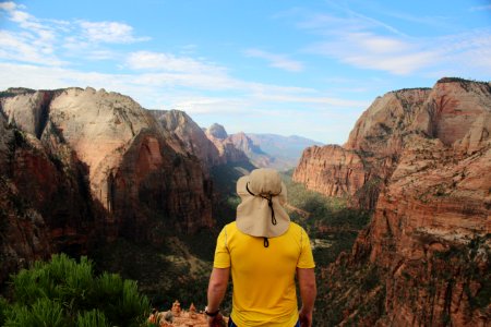 man wearing yellow shirt standing on edge of cliff facing rock formations photo
