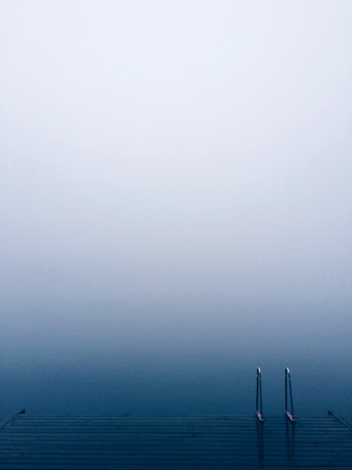 Lake pier with a ladder on serene waters on a foggy day
