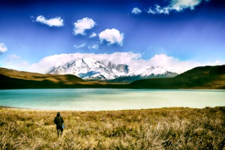 person standing on green grass with green calm body of water near mountains view at daytime photo